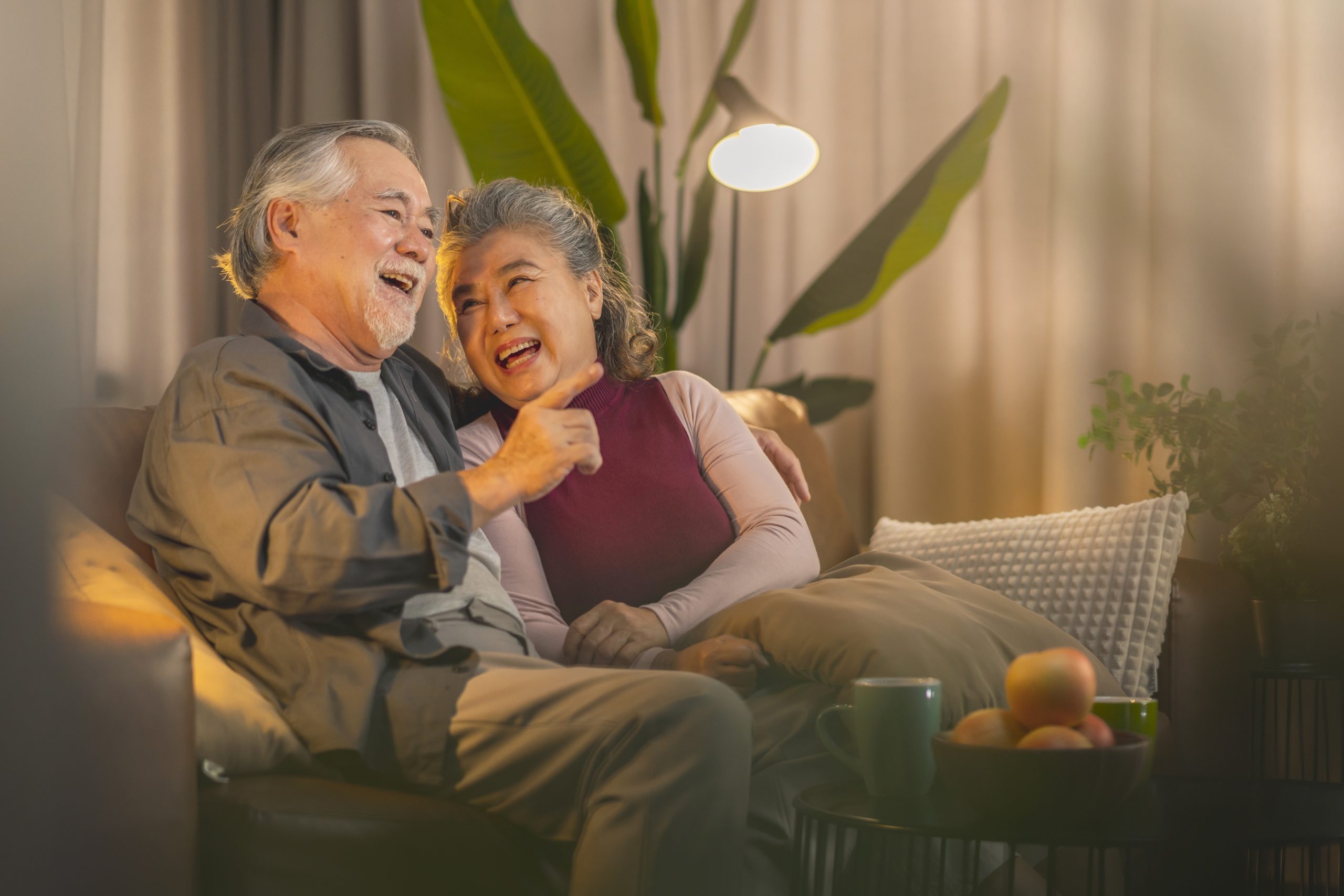 old retired age asian couple watching TV at home,old mature asian couple cheering sport games competition together with laugh smile victory on sofa couch at living room home isolation activity